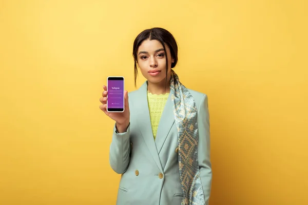 KYIV, UKRAINE - 4 FÉVRIER 2020 : belle fille afro-américaine tenant smartphone avec application instagram sur jaune — Photo de stock
