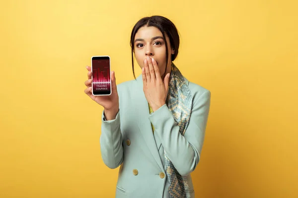 Shocked african american girl covering face and holding smartphone with trading curses on yellow — Stock Photo