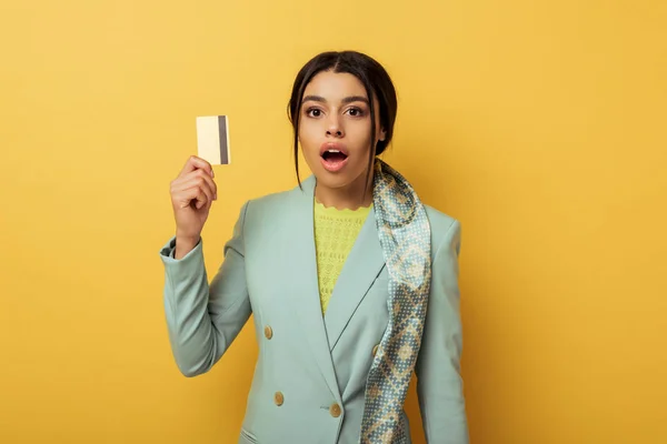 Surprised african american girl looking at camera and holding credit card on yellow — Stock Photo