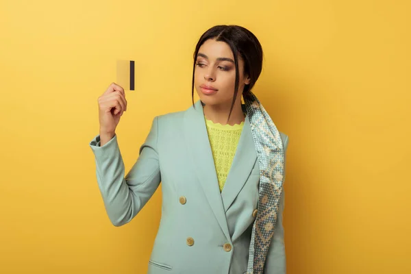 Pretty african american girl looking at credit card on yellow — Stock Photo