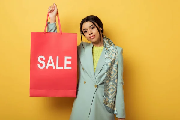 Attractive african american girl holding shopping bag with sale lettering on yellow — Stock Photo