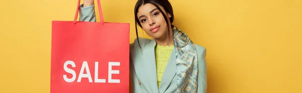 Panoramic shot of attractive african american girl holding shopping bag with sale lettering on yellow — Stock Photo