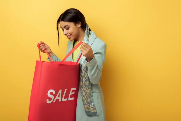 Cheerful african american girl holding shopping bag with sale lettering on yellow — Stock Photo