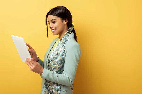 Mujer afroamericana feliz usando tableta digital en amarillo - foto de stock