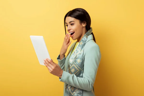 Mujer afroamericana feliz cubriendo la boca y mirando la tableta digital en amarillo - foto de stock
