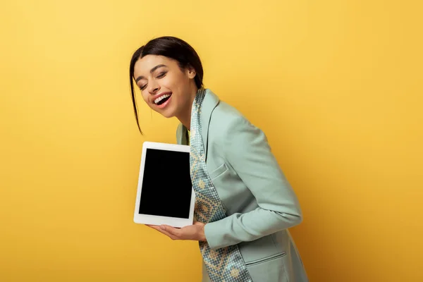 Happy african american woman holding digital tablet with blank screen and laughing on yellow — Stock Photo