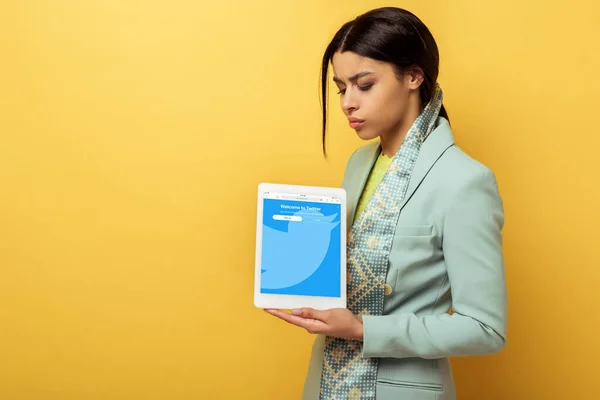 Femme afro-américaine mécontente tenant tablette numérique avec application twitter sur jaune — Photo de stock