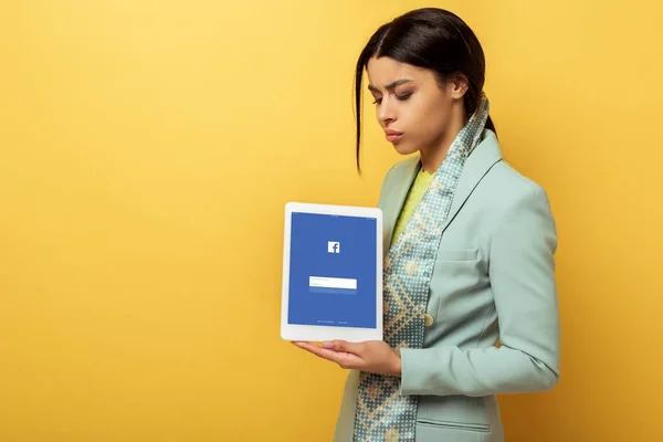 Displeased african american woman holding digital tablet with facebook app on yellow — Stock Photo