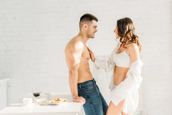 Sexy girl in white shirt and lingerie touching chest of sexy boyfriend in kitchen — Stock Photo