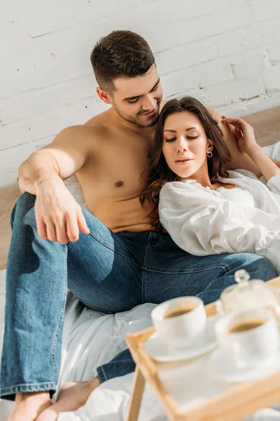 Enfoque selectivo de la feliz pareja joven cerca de la bandeja de la cama con desayuno - foto de stock