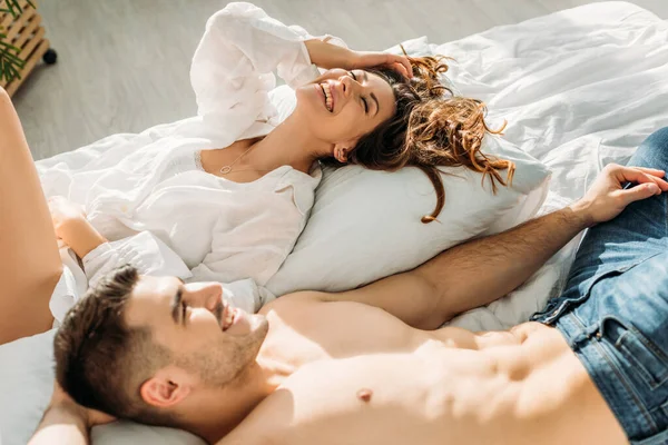 Vue aérienne de la jeune femme sexy et bel homme torse nu souriant tout en étant couché dans le lit — Photo de stock