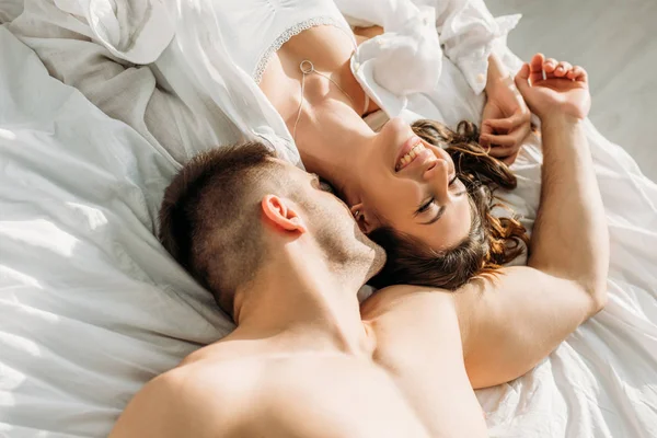 Vista aérea de hombre joven sin camisa acostado en la cama cerca de sexy, novia alegre - foto de stock