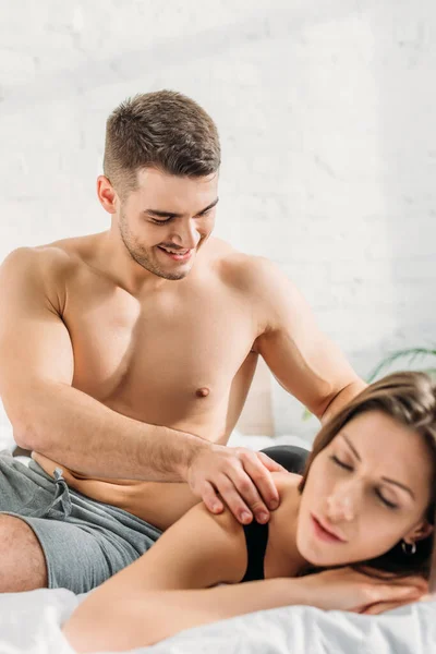 Foco seletivo de homem sexy fazendo ombros massagem erótica para namorada deitado e sorrindo com os olhos fechados — Fotografia de Stock