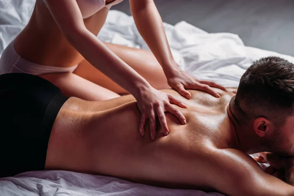 Обрезанный вид девушки, делающей обратно эротический массаж без рубашки бойфренд лежит на кровати — стоковое фото