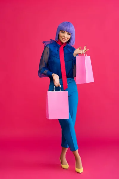 Fashionable girl in purple wig holding shopping bags, on pink — Stock Photo