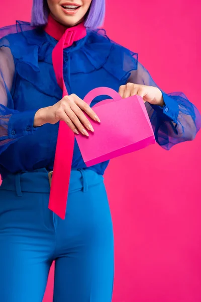 Обрізаний вид усміхненої стильної дівчини, що тримає маленький торговельний пакет, ізольований на рожевому — стокове фото