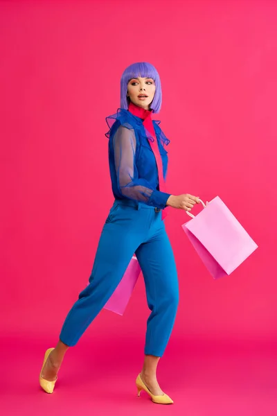 Fashionable shocked girl in purple wig holding shopping bags, on pink — Stock Photo