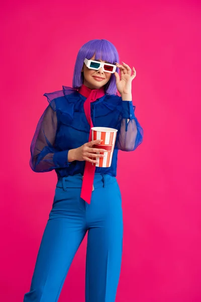 Happy pop art girl in purple wig and 3d glasses holding popcorn, isolated on pink — Stock Photo