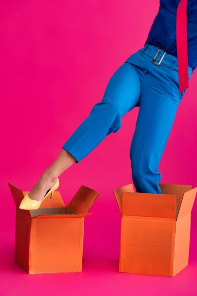 Cropped view of girl standing in cardboard boxes on pink — Stock Photo