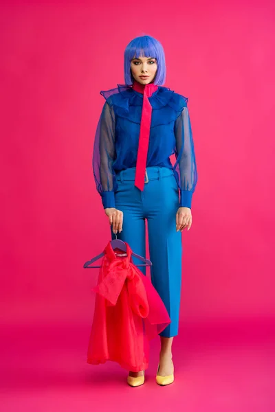 Menina bonita em peruca roxa segurando cabide com blusa vermelha, em rosa — Fotografia de Stock