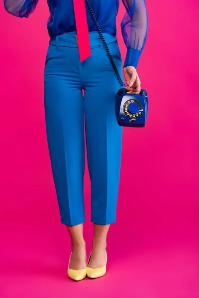 Vista recortada de la chica con estilo en pantalones azules con teléfono retro, en rosa - foto de stock