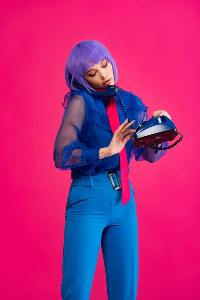 Fashionable attractive girl in purple wig talking on retro telephone, isolated on pink — Stock Photo