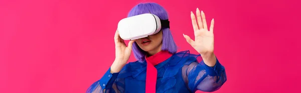 Панорамний знімок привабливої поп-арт-дівчини в блакитній блузці та фіолетовій перуці з використанням гарнітури віртуальної реальності, ізольованої на рожевому — стокове фото