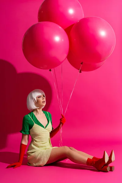 Bella ragazza scioccata in parrucca bianca che tiene palloncini su rosa — Stock Photo