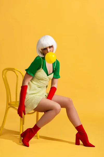 Beautiful pop art woman in white wig with bubble gum sitting on chair — Stock Photo