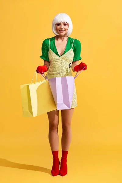 Smiling pop art girl in white wig holding shopping bags, on yellow — Stock Photo