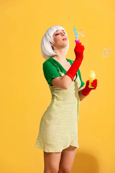 Schöne Pop-Art-Mädchen in weißer Perücke weht Seifenblasen, auf gelb — Stockfoto