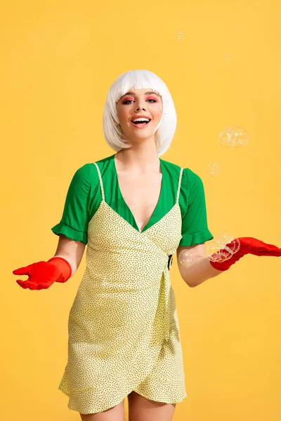 Attraente ragazza pop art felice in parrucca bianca con bolle di sapone, su giallo — Foto stock