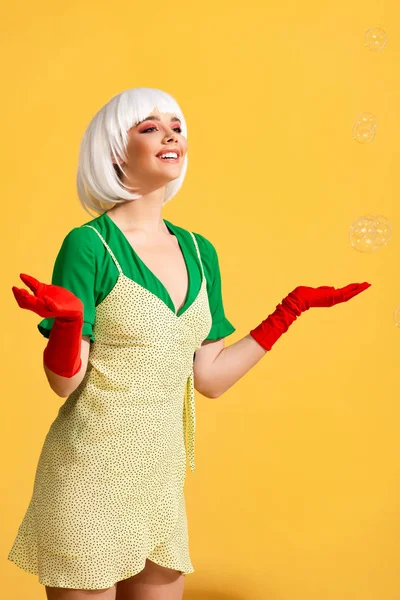 Attraktives lächelndes Pop-Art-Mädchen in weißer Perücke mit Seifenblasen, auf gelb — Stockfoto