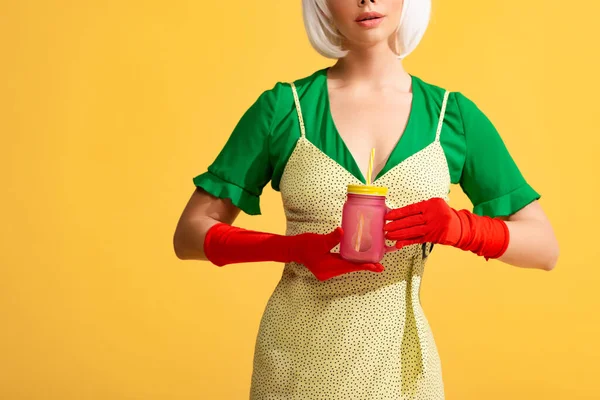 Vue recadrée de pop art fille en robe jaune et perruque blanche tenant pot avec boisson fraîche, isolé sur jaune — Photo de stock