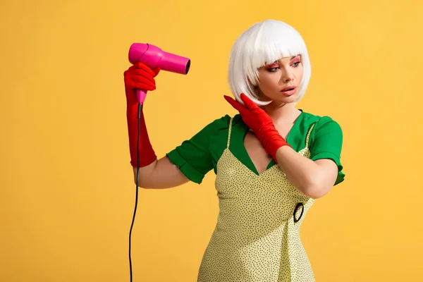 Pop art girl in white wig using hair dryer, isolated on yellow — Stock Photo