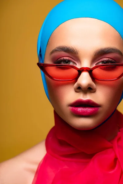 Hermosa chica de moda en bufanda de moda y gafas de sol rojas, aislado en amarillo - foto de stock