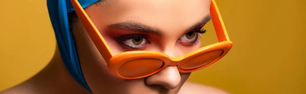 Panoramic shot of fashionable girl in scarf and trendy sunglasses, isolated on yellow — Stock Photo