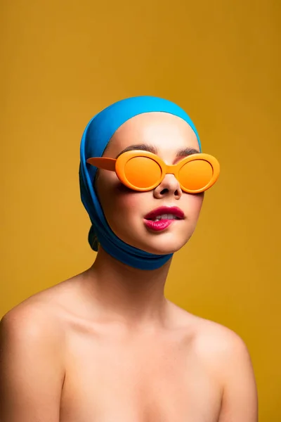 Chica desnuda de moda en bufanda y gafas de sol de color naranja que muerden el labio, en amarillo - foto de stock