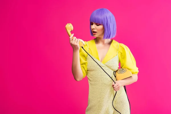 Mujer emocional en peluca púrpura sosteniendo teléfono retro, aislado en rosa — Stock Photo