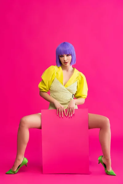 Sexy pop art girl in purple wig and yellow dress holding blank placard, on pink — Stock Photo