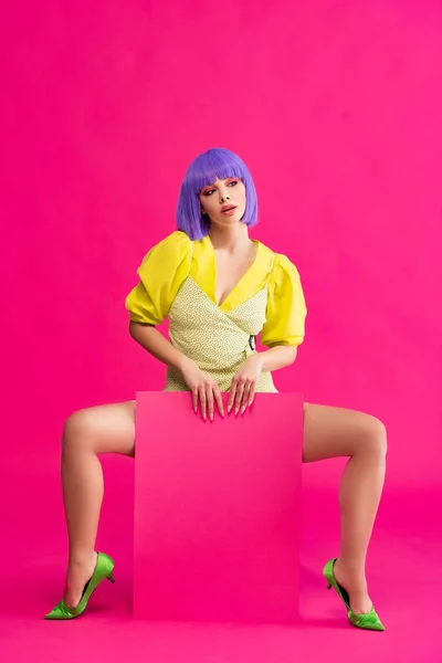 Seductive pop art girl in purple wig and yellow dress holding blank placard, on pink — Stock Photo