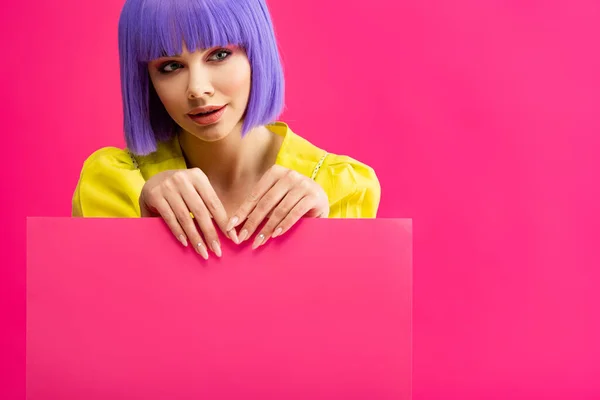 Sorridente pop art girl em peruca roxa segurando cartaz em branco, isolado em rosa — Fotografia de Stock