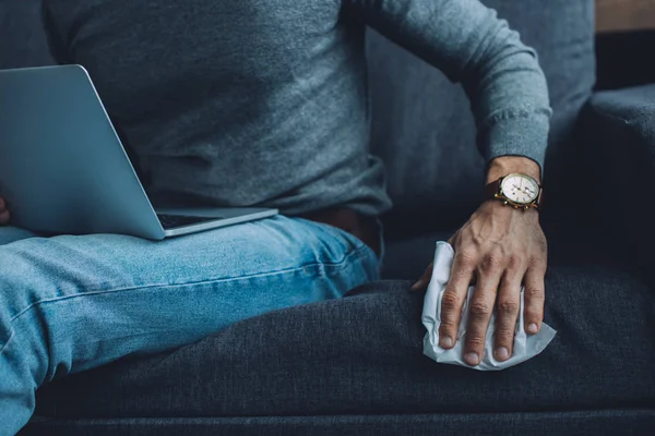 Cropped view of man holding napkin while watching pornography on laptop on couch — Stock Photo