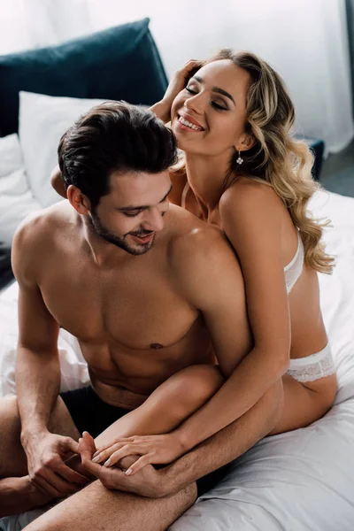 Sensuale donna sorridente toccando mano del fidanzato senza maglietta sul letto — Foto stock