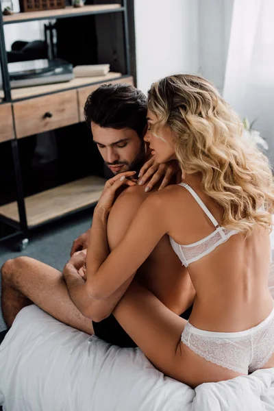 Vista posteriore di seducente donna in lingerie abbracciando bel fidanzato sul letto in camera da letto — Foto stock