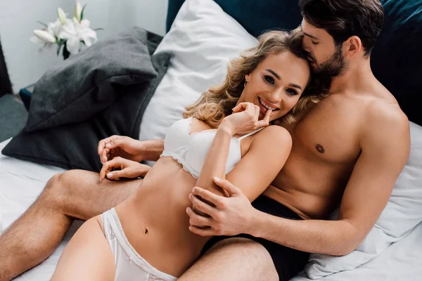 Schöner Mann umarmt verführerische Freundin lächelnd in die Kamera auf dem Bett — Stockfoto