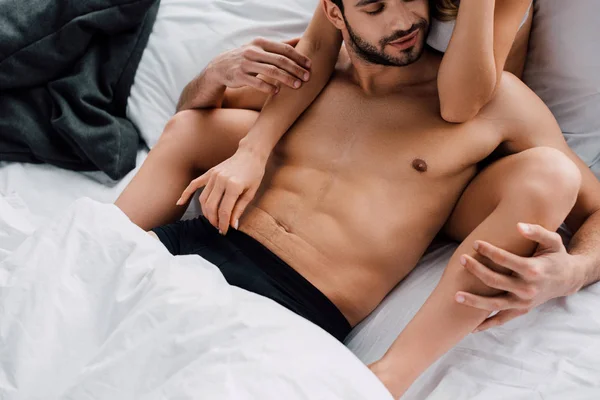 Muscular man touching girlfriend while lying on bed — Stock Photo