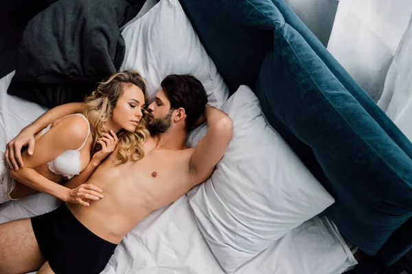 Top vista de homem bonito abraçando mulher sexy em lingerie enquanto deitado na cama — Fotografia de Stock