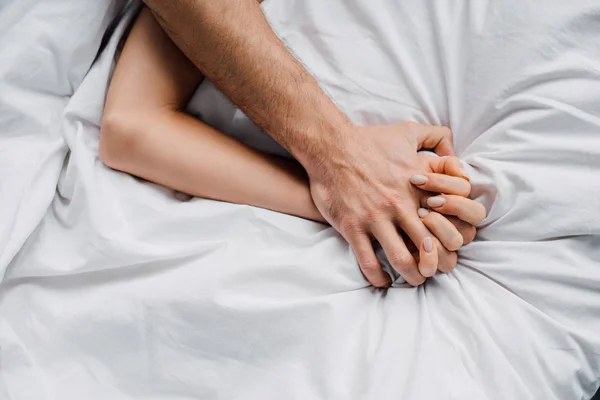 Vista superior de la mujer cogida de la mano del novio en la cama - foto de stock