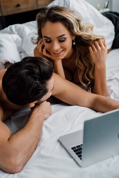 Selective focus of sexy woman looking at boyfriend near laptop on bed — Stock Photo
